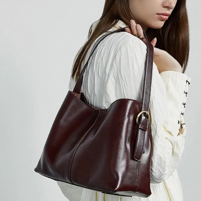 Woman in white blouse carrying burgundy leather shoulder bag with gold buckle