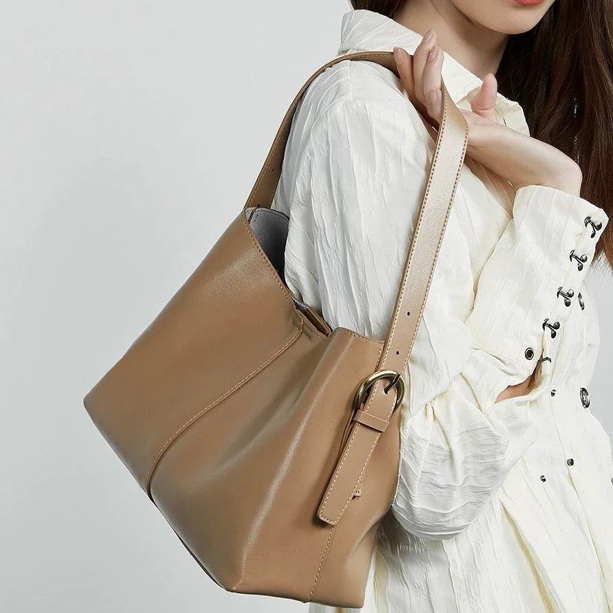 Beige leather tote bag with gold ring detail on woman's shoulder, white textured blouse