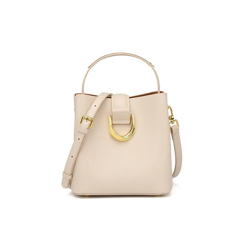 Beige leather handbag with gold buckle, top handle, and crossbody strap on white background