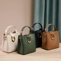 Four leather handbags in cream, green, black, and brown with gold accents on a wooden table