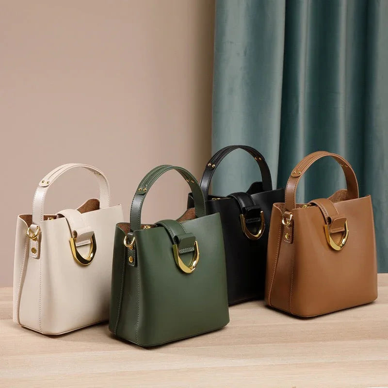 Four leather handbags in cream, green, black, and brown with gold accents on a wooden table
