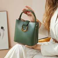 Woman in white suit holding green leather handbag with gold hardware indoors