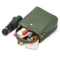 Green leather handbag with gold accents, open to show contents and a closed umbrella beside it