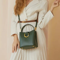 Woman in cream dress with brown belt holding green leather handbag with gold hardware