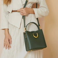 Woman in white outfit with pleated skirt holding a green leather handbag with gold hardware