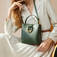 Woman in cream dress holding a green leather handbag with gold buckle, elegant fashion style
