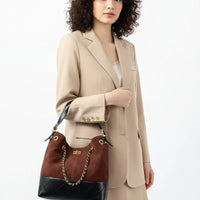Woman in beige blazer holding a brown and black quilted leather shoulder bag with chain strap