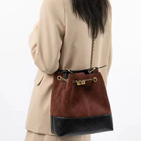 Woman in beige blazer carrying brown suede and black leather bucket bag with gold chain strap