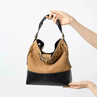 Brown and black leather shoulder bag with chain strap held by hands on white background.