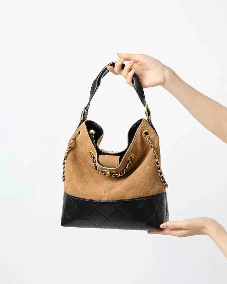 Brown and black leather shoulder bag with chain strap held by hands on white background.