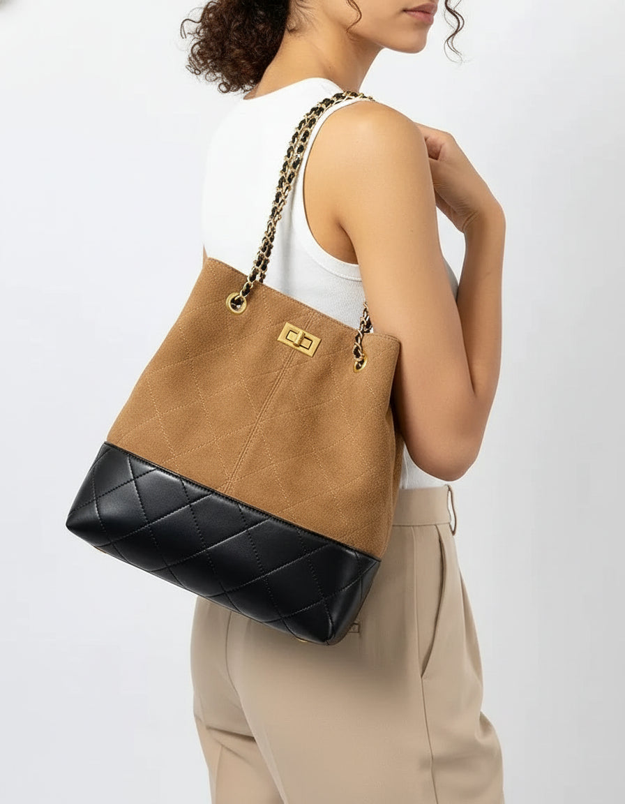 Woman wearing a tan and black quilted bucket bag with gold chain strap
