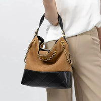 Woman holding a brown suede and black leather chain shoulder bag