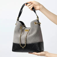 Gray and black quilted leather bucket bag with gold chain handle held by hand