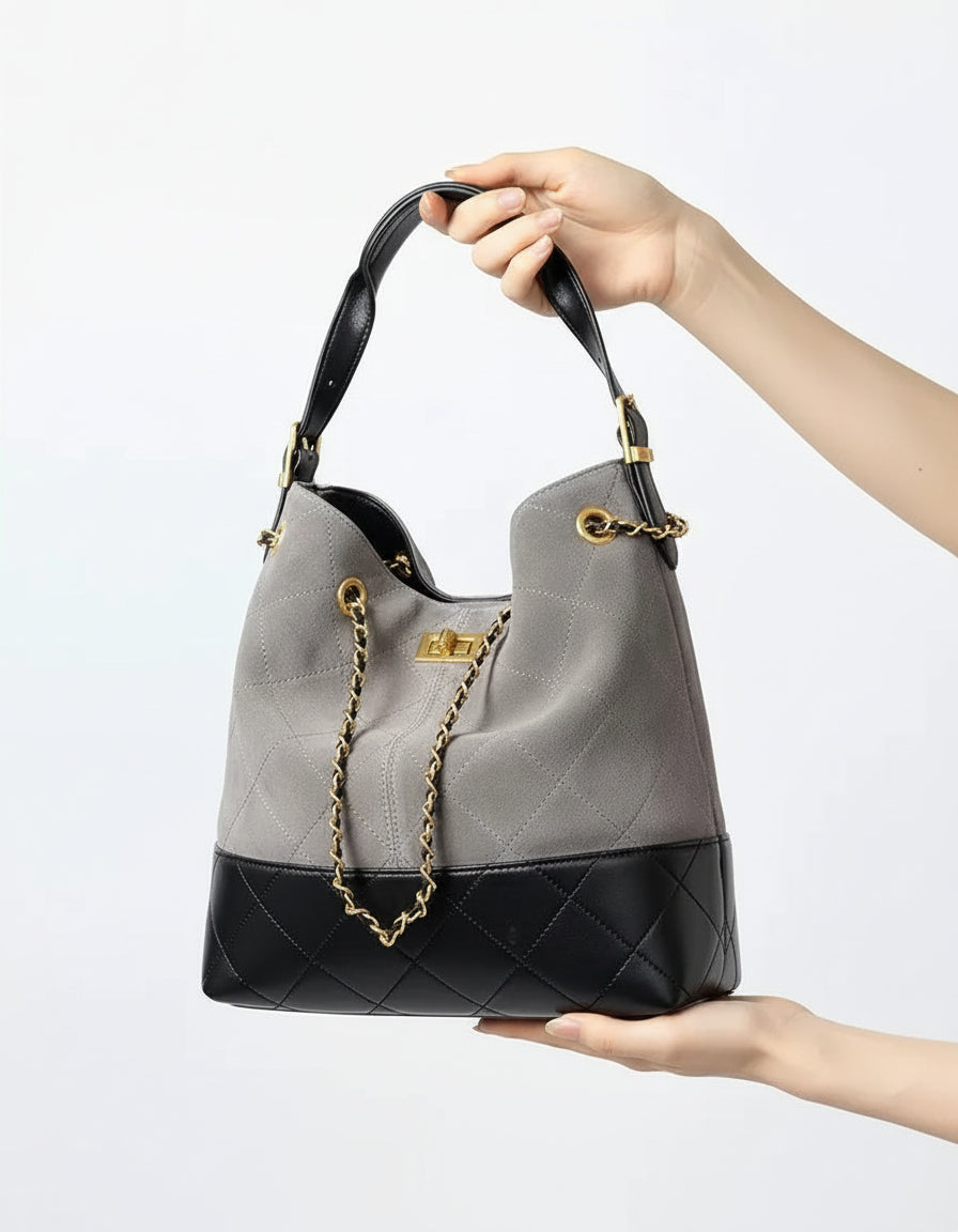 Gray and black quilted leather bucket bag with gold chain handle held by hand