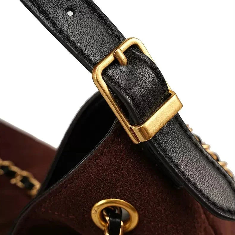 Close-up of a black leather bag strap with gold buckle and brown suede bag detail