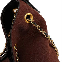 Brown suede handbag with gold chain strap and grommet detail, close-up view