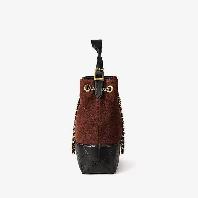 Side view of a brown suede bucket bag with black quilted leather base and gold chain strap
