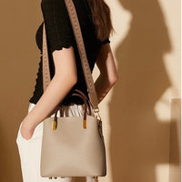 Woman wearing black top, white pants, and carrying a beige leather shoulder bag