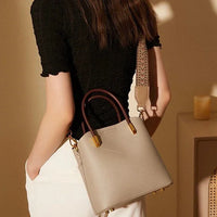 Woman with beige leather handbag, gold accents, and brown handles against neutral indoor background