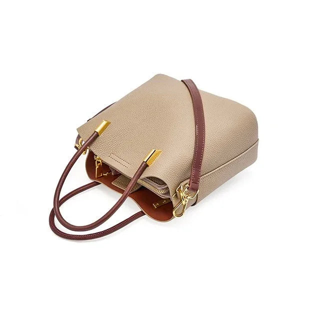 Beige leather handbag with gold hardware and brown straps on white background