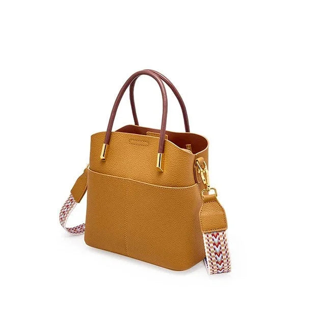 Tan leather tote bag with brown handles and woven multicolor shoulder strap on white background