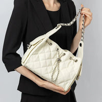 Woman in black blazer holding white quilted shoulder bag with chain strap