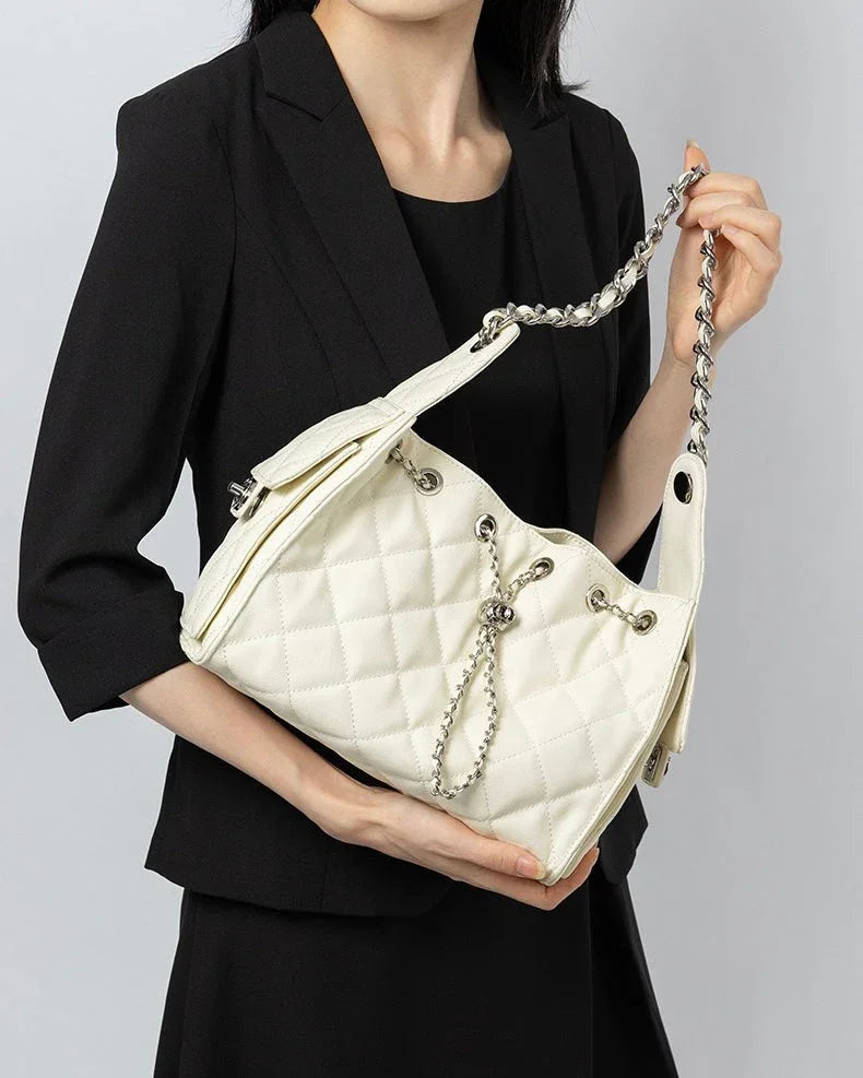 Woman in black blazer holding white quilted shoulder bag with chain strap