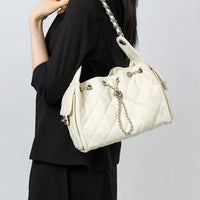 Woman in black outfit carrying white quilted shoulder bag with chain strap