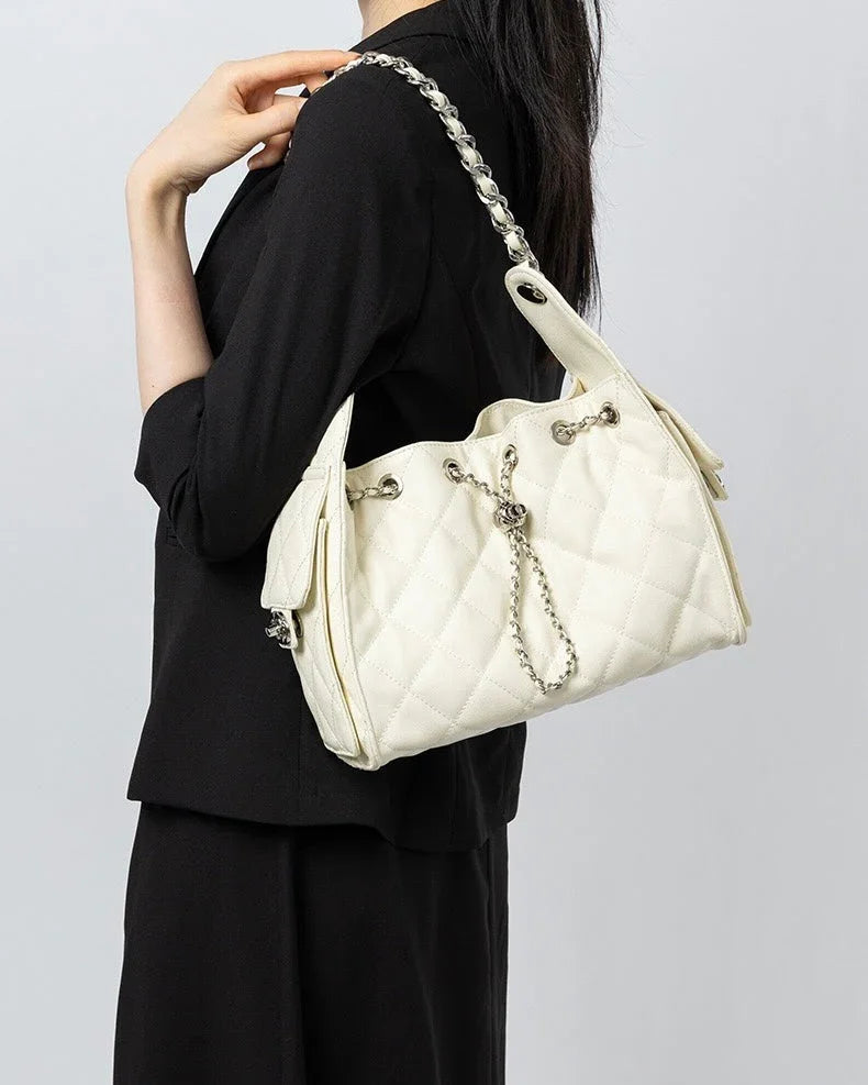 Woman in black outfit carrying white quilted shoulder bag with chain strap
