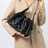 Woman in beige blazer holding black quilted leather handbag with chain strap