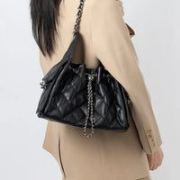 Woman in beige blazer carrying a black quilted leather shoulder bag with chain strap