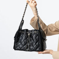 Woman holding black quilted leather handbag with chain strap and silver hardware