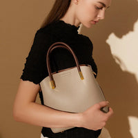 Woman holding a beige leather handbag with brown handles on a neutral background