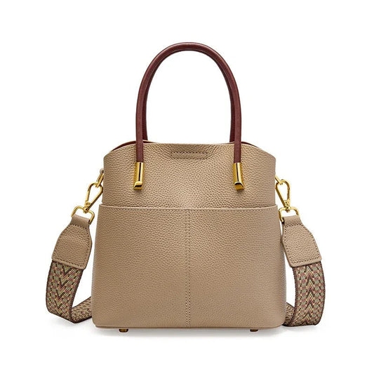 Taupe leather handbag with brown handles, gold hardware, and woven shoulder strap