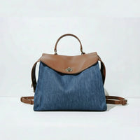 Denim backpack with brown leather flap, handle, and straps on white background