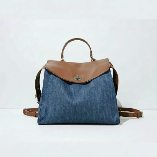 Denim backpack with brown leather flap, handle, and straps on white background