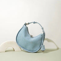 Light blue crescent-shaped shoulder bag with top handle on minimalist background