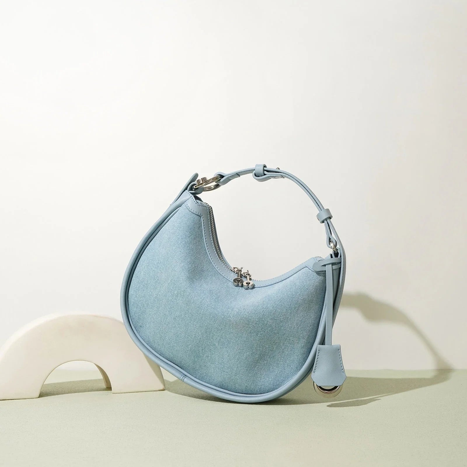 Light blue crescent-shaped shoulder bag with top handle on minimalist background