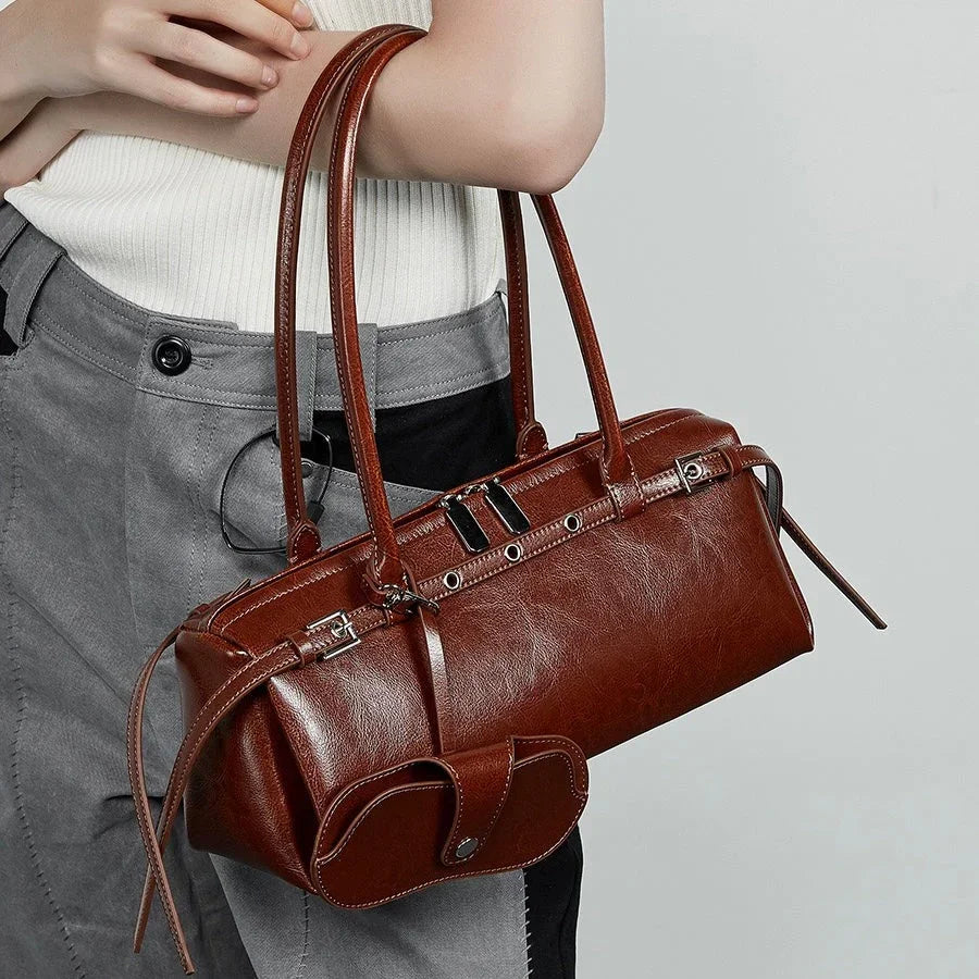 Woman holding brown leather handbag with double handles and silver hardware