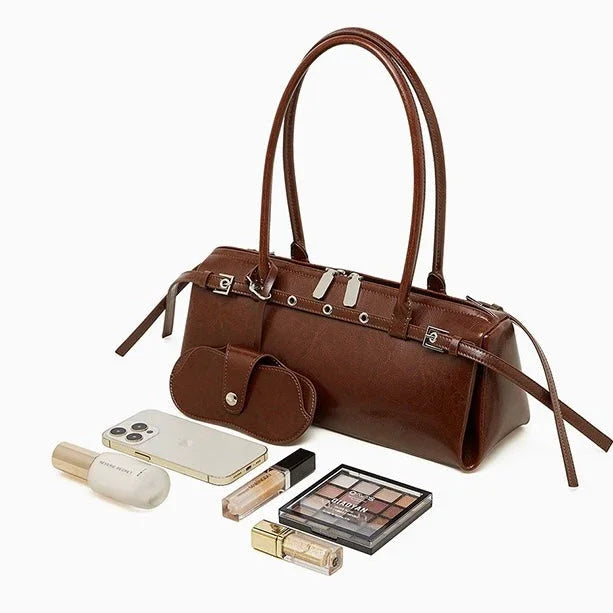 Brown leather handbag with makeup, smartphone, and wallet on white background