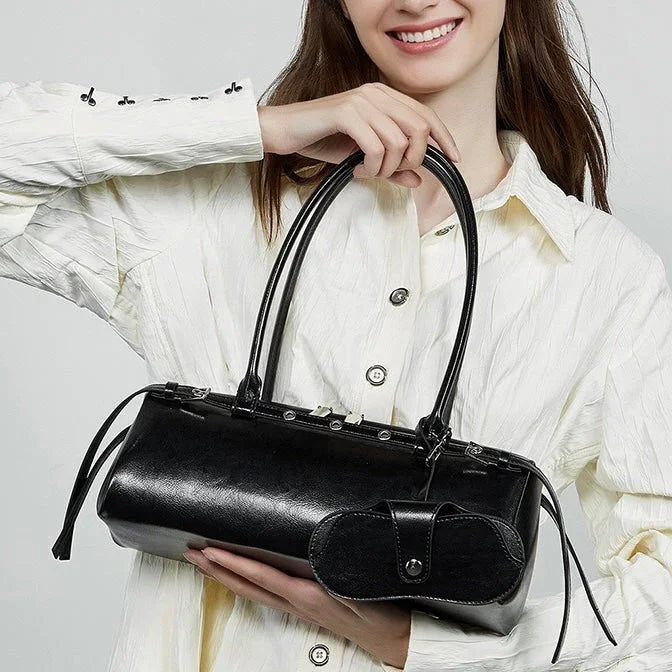 Woman in white shirt holding a black leather handbag with double straps and attached pouch