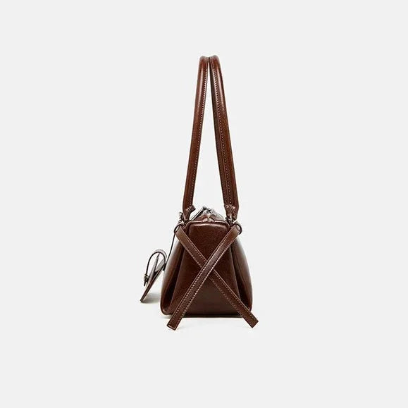 Side view of brown leather handbag with double handles and crossbody strap on white background