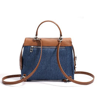 Denim and brown leather crossbody bag with top handle and zippered pocket on white background