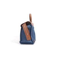 Side view of a blue denim and brown leather handbag with a zipper and handle