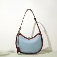 Light blue crescent shoulder bag with brown leather trim and adjustable strap on plain background