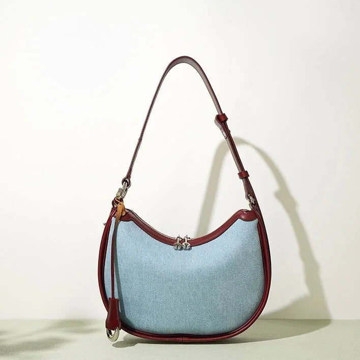 Light blue crescent shoulder bag with brown leather trim and adjustable strap on plain background