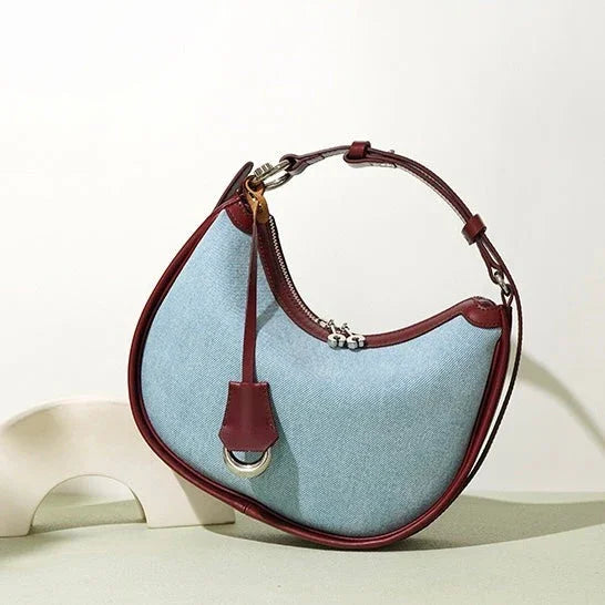Light blue crescent shoulder bag with maroon leather trim on a neutral background