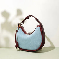 Light blue denim shoulder bag with maroon leather trim and strap on neutral background