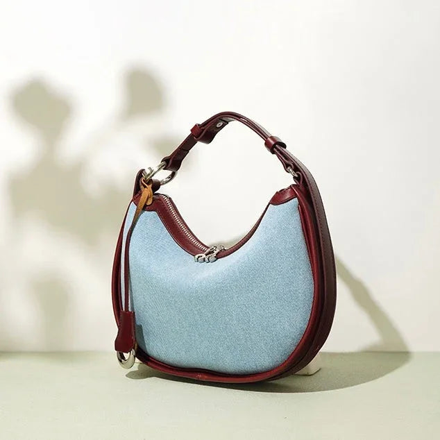 Light blue denim shoulder bag with maroon leather trim and strap on neutral background
