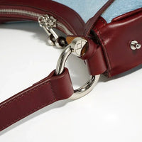 Close-up of a burgundy leather and denim handbag with silver hardware ring detail